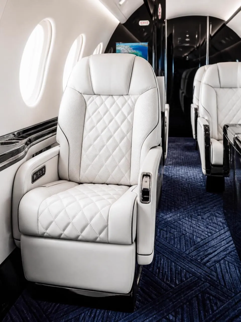 Private jet cabin with ivory diamond-quilted leather seats, polished black accents and deep navy patterned carpet