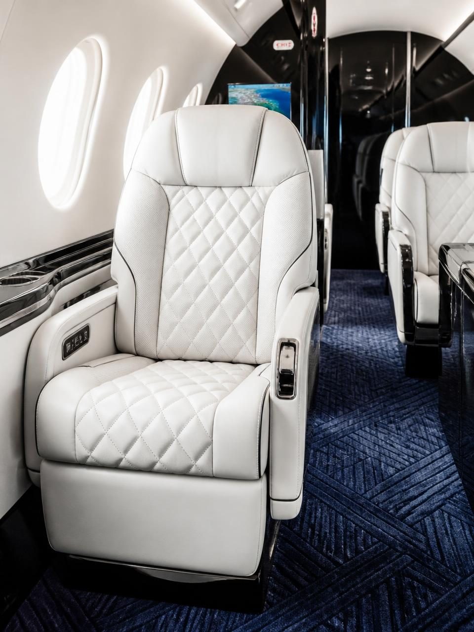 Private jet cabin with ivory diamond-quilted leather seats, polished black accents and deep navy patterned carpet